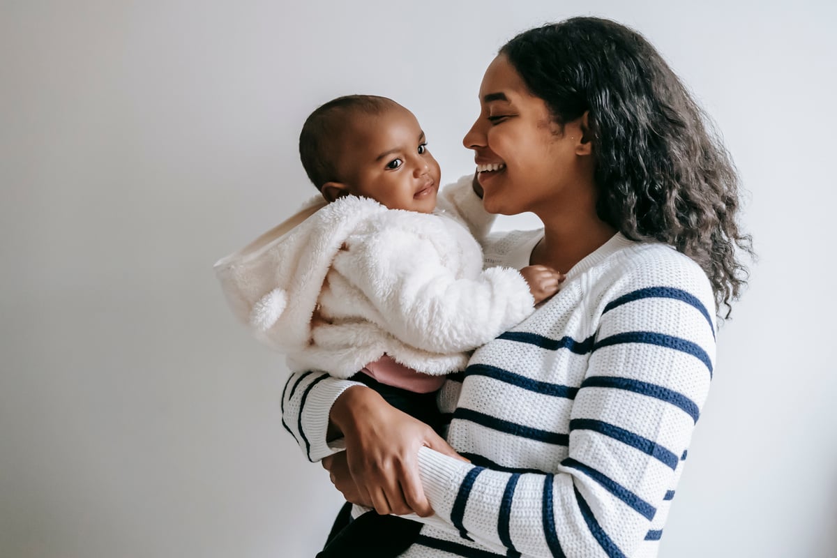 Indian mother hugging baby while holding in arms at home